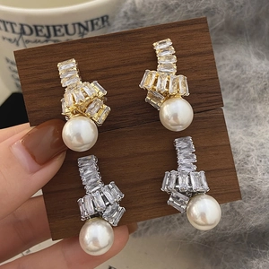 Vue détaillée de boucles d'oreilles nœuds or et argent avec cristaux carrés et perles