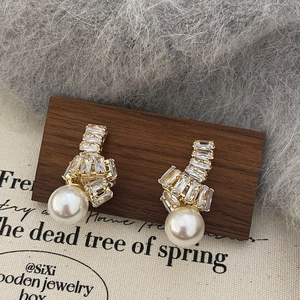 Détail de boucles d'oreilles dorées avec zircons rectangulaires et grandes perles