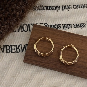Gros plan de créoles dorées avec émail marron et texture torsadée sur bois