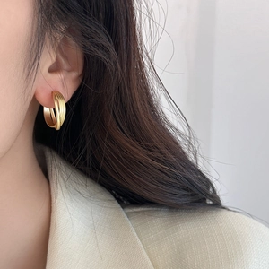 Boucles d'oreilles créoles entrelacées en or mat portées avec un blazer blanc élégant
