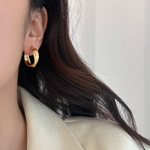 Détail de boucles d'oreilles géométriques dorées multicouches portées pour un style épuré