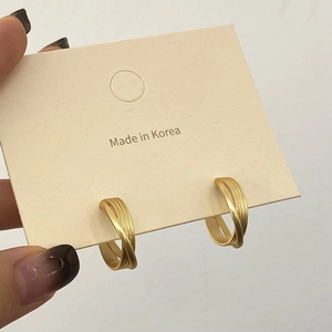 Détail de boucles d'oreilles dorées torsadées en C avec texture brossée mate sur carte