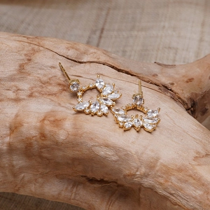 Élégantes boucles d'oreilles fleur dorées avec zircones marquise sur un support en bois