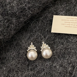 Detail of crown-shaped gold earrings with white pearls and sparkling zircon accents