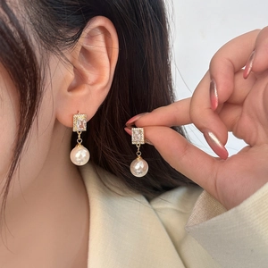 Elegant gold earrings with emerald-cut zircon and round white pearl worn by a model