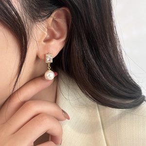 Close-up of elegant gold drop earring featuring a rectangular zircon and white pearl