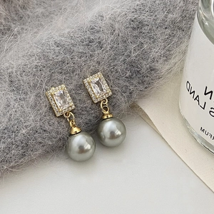 Macro detail of gold earrings featuring gray pearls and zircon stones on soft plush fabric