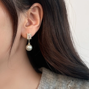 Elegant gold drop earrings with white pearl and rectangular zircon on female model