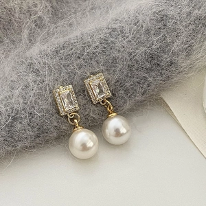 Detailed close-up of golden pearl drop earrings with sparkling rectangular zircon studs