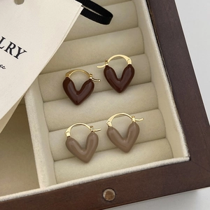 Close-up of heart-shaped enamel earrings in brown and tan tones on beige velvet