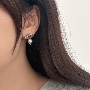 Gros plan d'une boucle d'oreille nœud argentée avec perle blanche sur l'oreille d'un modèle