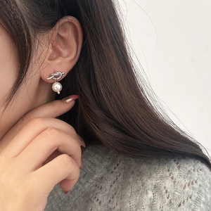 Détail de boucle d'oreille nœud argenté avec perle portée sur l'oreille du modèle