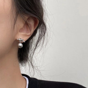 Gros plan de boucles d'oreilles nœud argentées avec perle pendante sur un modèle