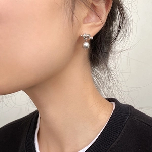 Détail de boucles d'oreilles nœud argenté avec perle grise portée par un modèle