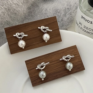 Détail de boucles d'oreilles nœuds argentés avec perles blanches et grises sur supports