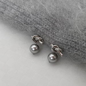Boucles d'oreilles nœud argenté avec perles grises sur fond doux texturé