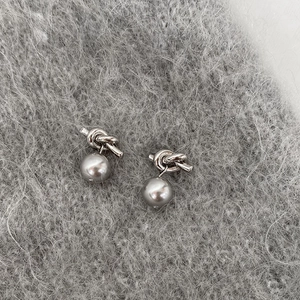 Détail de boucles d'oreilles nœud argentées avec perles grises sur tissu tricoté