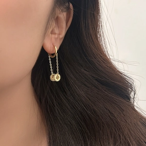 Detailed view of gold chain drop earrings with CD logo pendants worn by a model
