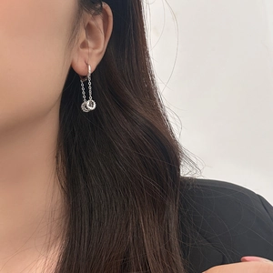 Detail view of silver drop earrings with chains and gear charms on a model's ear