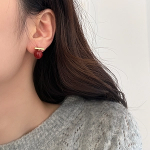 Élégantes boucles d'oreilles perles rouges et barre dorée portées par un mannequin