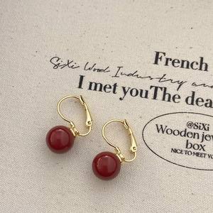 Détail de boucles d'oreilles à breloques rouges avec crochets français dorés sur toile