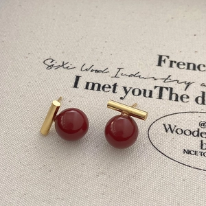 Détail de boucles d'oreilles perles rouges avec tiges dorées sur fond de toile beige