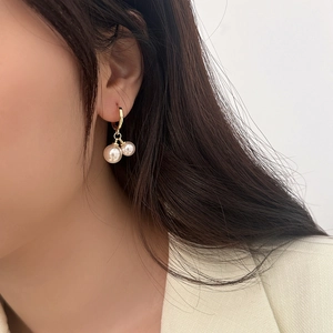 Elegant gold hoop earrings with double pearl pendants shown on a model