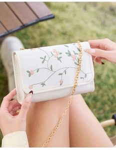Détail du sac blanc rectangulaire avec broderie florale rose et fine chaîne dorée