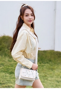 Détail du sac bandoulière blanc avec broderie florale et chaîne dorée sur modèle