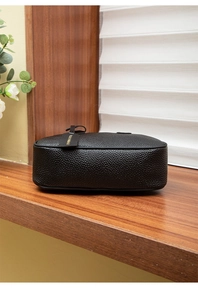Detail of black lychee grain leather texture with gold logo tag on a wooden surface
