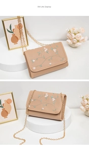 Détail de la broderie florale sur le rabat et chaîne dorée du sac à bandoulière beige clair