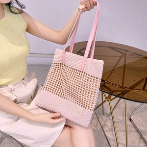Pink woven crochet shoulder bag with leather handles shown in a lifestyle indoor setting