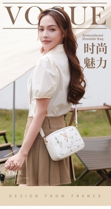 Detailed view of floral embroidery and gold butterfly on white camera bag with strap