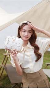 Detail of white square camera bag with floral embroidery and gold buckle hardware
