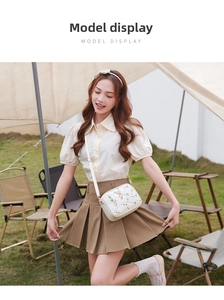 Outdoor model display of a white crossbody bag with floral and butterfly embroidery