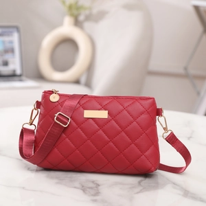 Detail of red quilted crossbody bag with golden metal plate on white marble surface