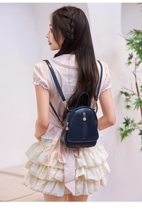 Close-up of a mini dark blue glossy PU leather backpack with silver metal zipper details