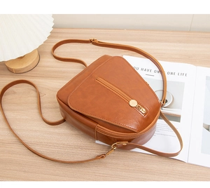 Detailed close-up of brown faux leather crossbody bag with a golden circular zipper ring
