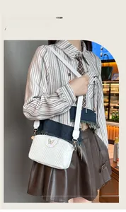 Detail of white quilted camera bag featuring golden butterfly logo and wide woven strap