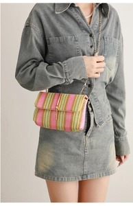 Close-up of pink and green woven straw crossbody bag with golden chain and metal bar