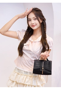 Detail of a black faux crocodile leather mini bag with gold chain and tassel decoration