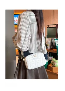 Detail of white chevron quilted camera bag with golden butterfly metal ornament