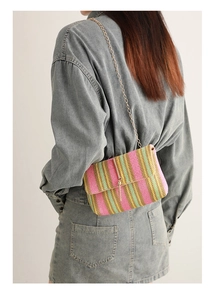 Rainbow striped woven crossbody bag with gold chain strap shown on a denim outfit