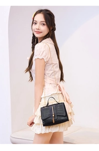Detail of black faux crocodile leather crossbody bag with gold chain and metal tassel