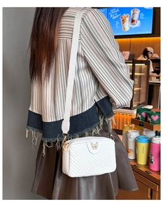 Detailed close-up of white quilted camera bag with elegant gold butterfly clasp