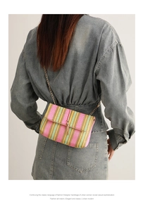 Detail of colorful woven crossbody bag with gold chain strap on denim dress background