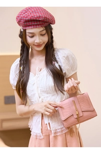 Detail of pink croc-effect handbag featuring a gold tassel metal buckle and chain strap