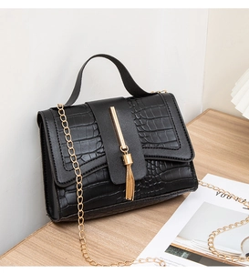 Detailed macro shot of the black crocodile texture and gold tassel on the handbag