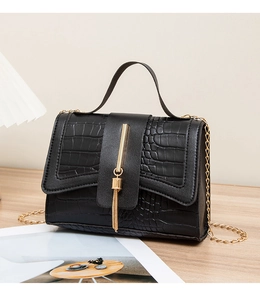 Close-up of black crocodile pattern leather bag with gold metal bar and tassel detail