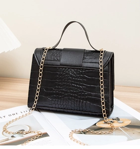 Detail of black crocodile embossed leather texture and gold metal chain strap of the bag
